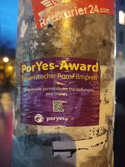 Street sticker Sticker promoting the PorYes-Award, a feminist porn film award.  The sticker features the award's name, a description in German ("Feministischer PornFilmpreis", which translates to "Feminist Porn Film Award"), a tagline ("Respectful pornographic depictions are possible"), and a QR code linking to poryese.  The design uses a purple color scheme with white text.