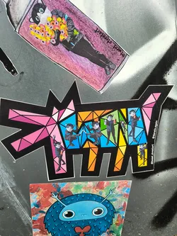 This sticker shows a geometric interpretation of a dog, segmented into colorful triangular shapes. Each section contains a repeated image of a masked individual.  The style is bold and graphic.  The artist's Instagram handle is visible on the sticker.