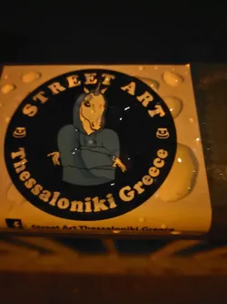 Street sticker Round sticker featuring a unicorn wearing a hoodie. The sticker has a black background with white and yellow text.  The text says "Street Art" at the top, "Thessaloniki Greece" wrapped around the bottom, and has a small facebook logo at the bottom.