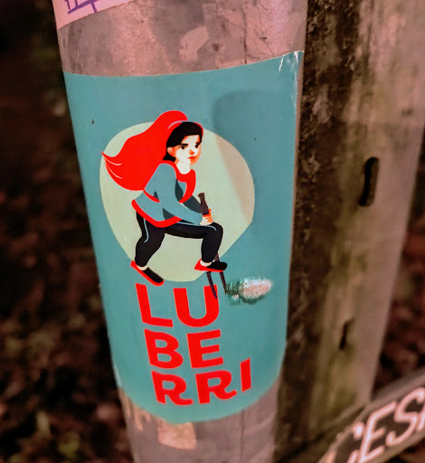 Street sticker A teal sticker featuring an illustration of a person with red hair and a teal jacket, striding with what appears to be trekking poles. Below the illustration is the word "LUBERRI" in red lettering.