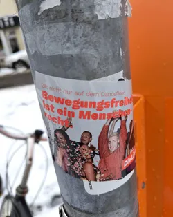 A sticker featuring a group of joyful people amidst confetti, with the statement "Bewegungsfreiheit ist ein Menschenrecht" (Freedom of movement is a human right) prominently displayed.  The text indicates that this right applies beyond just dance floors.