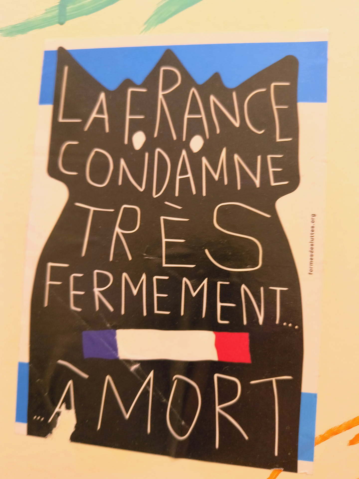 Street sticker The sticker is predominantly black with white, hand-drawn style text. Its overall shape is irregular, resembling a silhouette with a jagged, crown-like top edge, behind which a strip of blue is visible. A horizontal band in the middle displays the French flag colors: blue, white, and red. The text is arranged in several lines, with a website URL printed vertically along the right edge. The sticker appears to be slightly worn or peeling at the bottom left corner, indicating it's a physical object on a surface.