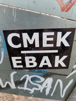 A black and white sticker with the text CMEK over EBak. The sticker shows some signs of wear.
