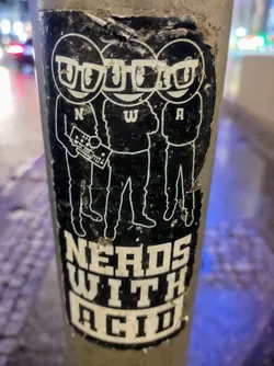 A sticker featuring three cartoon nerds with glasses, holding a synthesizer. The text 'Nerds With Acid' is displayed at the bottom.