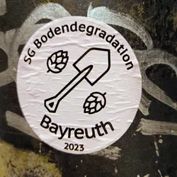 A round sticker with a shovel and hop icons. The text on the sticker says: SG Boden degradation Bayreuth 2023.