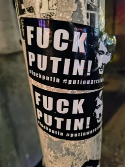 Street sticker Two black and white stickers plastered on a pole. The stickers read "FUCK PUTIN!" with hashtags #fuckputin and #putinwarcriminal. There's also a cutout of Putin's head on the right side of the sticker.