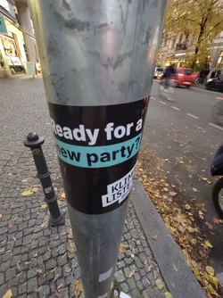Street sticker A black and teal sticker on a pole. The sticker has the text "Ready for a new party?" and a logo that says "KLIMA LISTE" in a sans-serif font. There is no QR code or social media links visible.