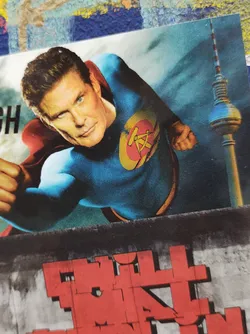 This sticker showcases a stylized superhero figure, reminiscent of Superman but with a significant alteration: their emblem appears to be a stylized version of the hammer and sickle symbol, often associated with communism. The background includes a blurred image of the Berlin Television Tower, adding a layer of context and visual intrigue. The overall aesthetic is striking and unconventional. 