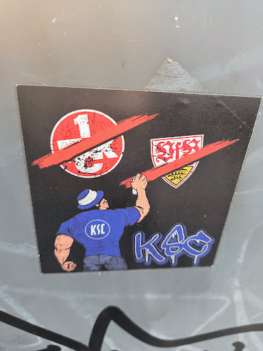 Street sticker The sticker features a man in a blue shirt with 'KSC' on the back, who is using a red spray can to paint over the logos of 1. FC Kaiserslautern and VfB Stuttgart. This symbolizes rivalry between the teams.