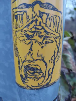Street sticker This sticker showcases an expressive face with intense features. The style is reminiscent of woodcut prints or linocuts, with strong lines and shading creating a textured effect. The color combination of yellow and blue is eye-catching, giving the sticker a vintage or retro feel. There is no visible text or QR code on the sticker itself.