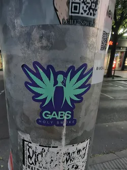 Street sticker A die-cut sticker depicting a green silhouette of a smoking figure with cannabis leaf wings on a dark purple background. The text 'GABS' and 'HOLY SMOKE' is printed below.