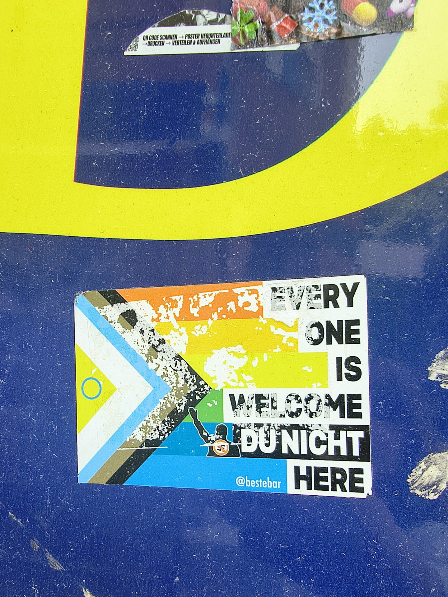 A weathered rectangular sticker combining the Progress Pride flag with anti-fascist messaging. It features the text 'EVERY ONE IS WELCOME DU NICHT HERE' alongside a silhouette of a Nazi-saluting figure crossed out. The handle '@bestebar' is printed at the bottom.