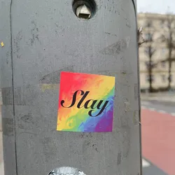 A square sticker with a rainbow background and the word "Slay" written in black cursive letters. The rainbow is styled as a marble or watercolor effect.