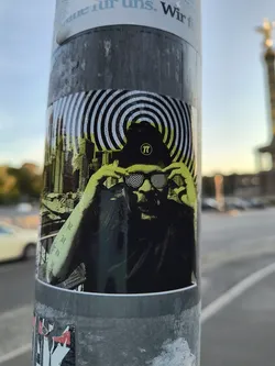 This sticker showcases a striking black and yellow image of a person with their eyes covered by hands.  The hat displays the mathematical symbol for pi. The background includes hypnotic concentric circles and a city skyline. The style is reminiscent of psychedelic art and urban aesthetics.
