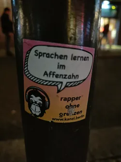 Street sticker A sticker featuring a monkey wearing headphones and text that says "Sprachen lernen im Affenzahn" (Learn languages quickly) and "rapper ohne grenzen" (rapper without borders).  A website address is also included.