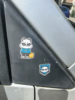 Street sticker Two die-cut stickers on black plastic. The upper sticker depicts a full-body cartoon panda with an angry expression, wearing a blue hoodie and grey pants. The lower sticker is a shield-shaped logo featuring the panda's face, branded with 'CASEKOO' and 'SPACE USER'.