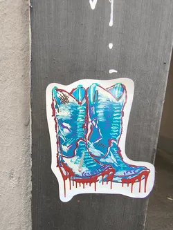 Street sticker A die-cut sticker depicting a pair of blue and teal cowboy boots. The design features sketchy outlines, purple highlights, and a prominent dripping red paint effect along the soles.