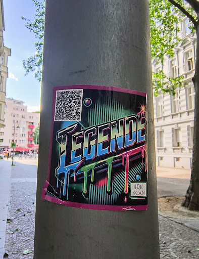 Street sticker A sticker featuring the word 'TEGENDE' in a stylized, dripping font is affixed to a gray pole. The word is rendered in shades of blue and black, with the dripping effect highlighted in green and pink. The sticker has a black background with white stripes. A QR code sits in the top left corner, and the text '40K SCAN' is visible in the bottom right corner. The sticker has a pink border.