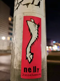 Street sticker A red sticker with a black and white illustration of what seems to be a stylized leg or hoof. The artist's name, nelly ZIEGENBEIN, is printed at the bottom.