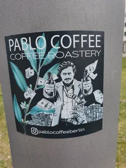 Street sticker Sticker featuring an illustration of Pablo Escobar holding guns surrounded by money and coffee plant. The sticker is black and white with teal accents. It has the Instagram handle @pablocoffeeberlin at the bottom.