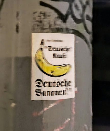 A sticker featuring a stylized illustration of a banana.  The text at the bottom appears to say "Deutsche Bananen" which translates from German to "German Bananas". There is additional, unclear text at the top of the sticker.