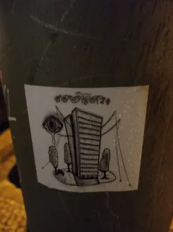 Street sticker Black and white drawing of a tall building with small trees around it, and a crying eye watching over it. The style is surreal and somewhat melancholic. It's stuck on a pole outside.