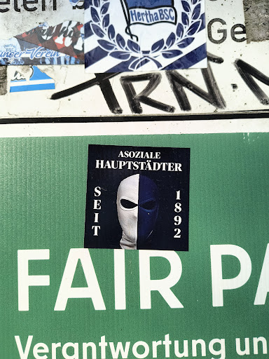 Street sticker The sticker shows the text "ASOZIALE HAUPTSTÄDTER SEIT 1892" above an image of a mask divided vertically, one half white and the other dark blue. The text translates to "Antisocial Capital Citizens Since 1892."