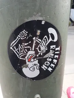 Round black and white sticker depicting a skeleton playing a trumpet. The text on the sticker says "Tiefen Rausch" which translates from German to "Deep intoxication".