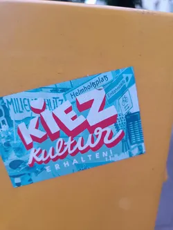 Street sticker A sticker promoting the preservation of Kiez culture. It features the text "Kiez Kultur erhalten!" in a stylized font, along with images and street names like Helmholtzplatz and Einbahnstraße. The design uses a teal and pink color scheme with a collage-like aesthetic.
