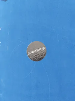 Street sticker A round, metallic silver sticker with the text "gorbatSHOW" in white on a blue surface.