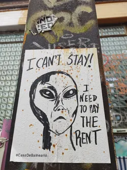 A sticker featuring a drawing of an alien's face with text that says "I can't stay! I need to pay the rent."  The sticker has some rust spots. The hashtag #CasaDeBalneario is visible at the bottom.
