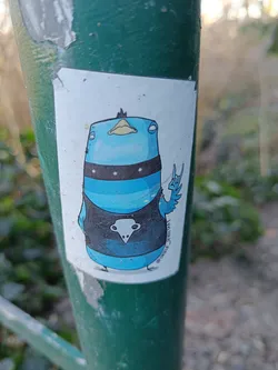 Street sticker A sticker featuring a cartoon illustration of a blue bird wearing a black shirt with a skull motif and making a rock and roll hand gesture. The style is reminiscent of cartoon illustrations often found in sticker art and street art. 