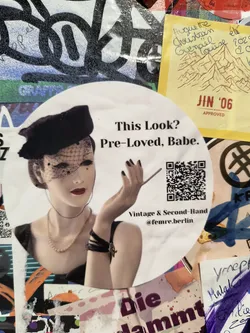 Street sticker A circular sticker featuring a stylized image of a mannequin or model wearing a black cloche hat with a veil, a pearl necklace, and a black dress. The model has red lipstick and is holding a cigarette. To the right of the model is a QR code. Below the QR code, the text 'Vintage & Second-Hand @femre.berlin' is visible. The sticker has a slightly aged appearance.