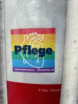 Street sticker A rainbow-colored heart with the word "Pflege" (German for "care") in the center.  The sticker promotes the hashtag #AufstandStattApplaus and includes an Instagram link to @jungePflege_dbfk. 