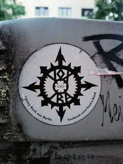 Street sticker Round sticker with a black and white symbol resembling a compass or a stylized star.  The text around the symbol says "Heavy Rock aus Berlin" and includes a Facebook link. The central symbol contains what looks like the letters "VXR" within a circular design.