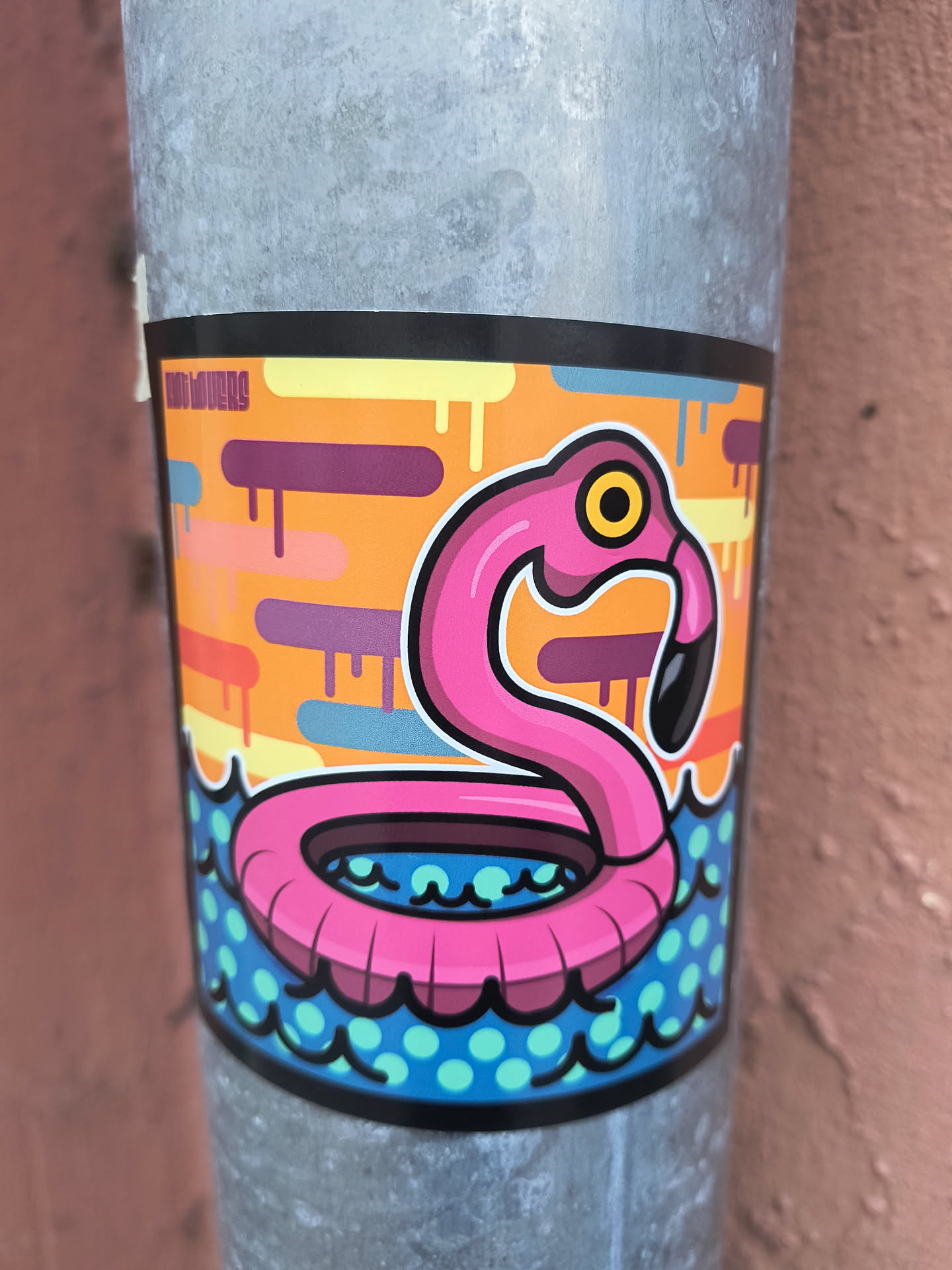 A colorful sticker featuring a stylized, bright pink flamingo head and neck, shaped like a pool float. The flamingo has a yellow eye with a black pupil and a black beak. It is depicted floating in blue water with light blue polka dots and dark blue wavy lines. The background above the water is a vivid orange, adorned with various abstract, rounded, dripping shapes in shades of purple, light orange, yellow, and light blue. The entire design is outlined with a bold black border.