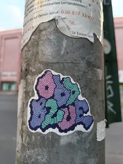 A sticker with the word 'love' designed using pastel color swirls.  The word is formed by the pattern itself. It's affixed to a grey pole outdoors.