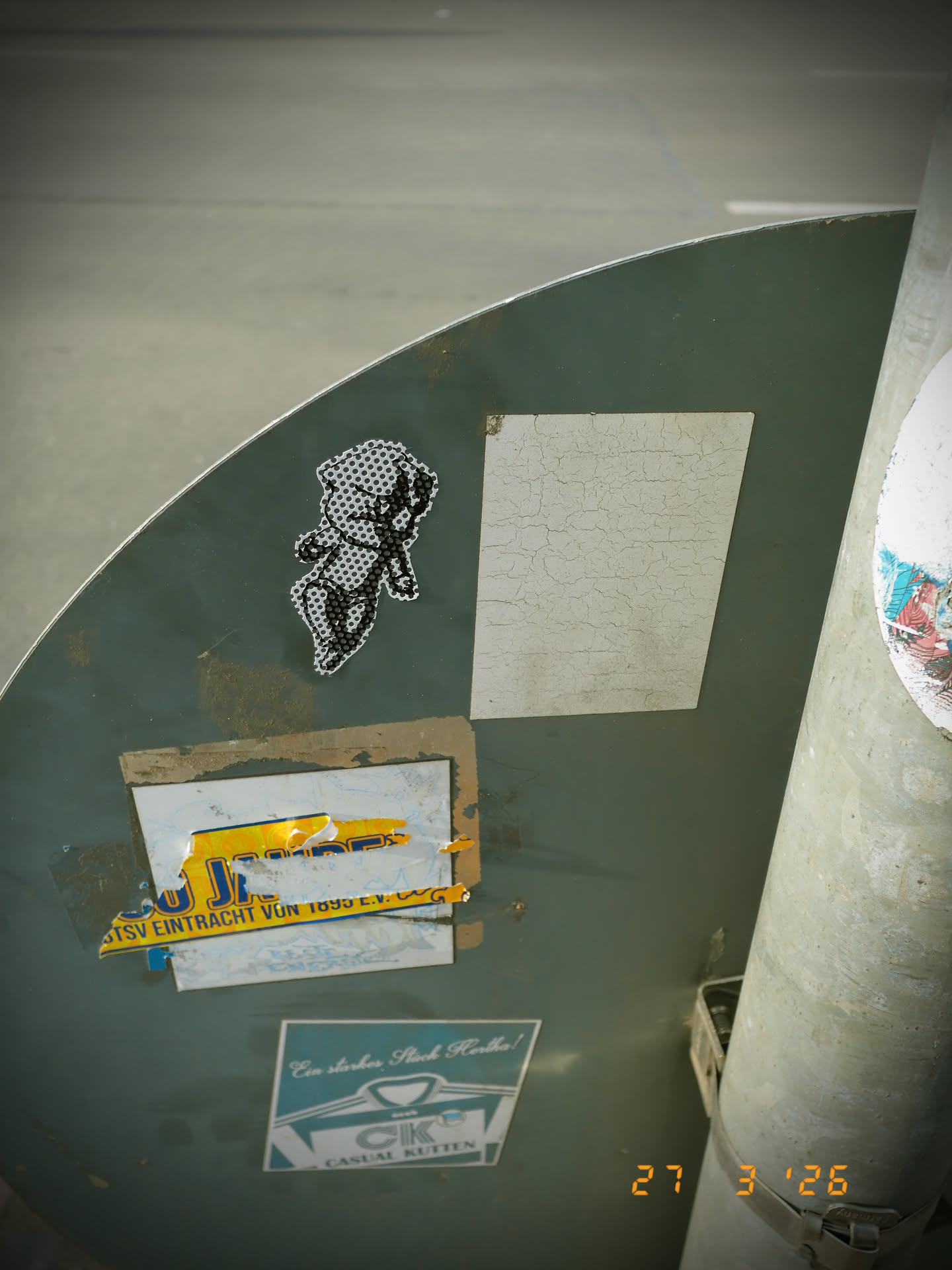 The sticker features a stylized, monochrome figure rendered entirely in a black and white halftone or polka-dot pattern. The figure appears to be a human-like character in a dynamic pose, possibly walking or dancing, with arms and legs outstretched. The design uses black dots on a white background to create the form and shading, giving it a pixelated or perforated appearance. The sticker is die-cut to the irregular outline of the figure, adhering to a dark green, curved surface.