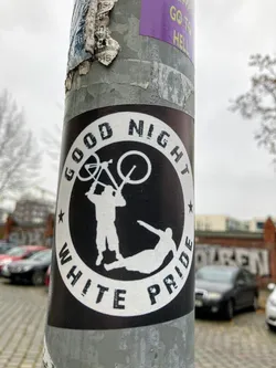 Street sticker A circular sticker with a stark black background and a white outer border. Inside the black circle, two stylized white figures are depicted. One figure stands upright, holding a bicycle overhead, seemingly in an act of aggression or confrontation towards a second figure that lies prone on the ground. The phrase 'GOOD NIGHT' is arched in white uppercase letters across the top inner part of the white border, and 'WHITE PRIDE' arches along the bottom. Small white stars are positioned on either side, separating the top and bottom text from the central imagery.