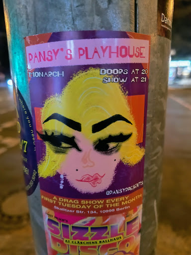 Street sticker This sticker advertises "Pansy's Playhouse", a drag show every first Tuesday of the month at Clärchens Ballhaus. The sticker features a face with striking makeup and blonde hair. The doors open at 20:00 and the show starts at 21:00.