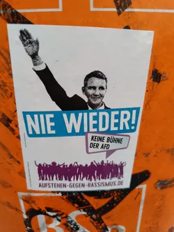 Street sticker A sticker featuring a stylized image of a person raising their arm in a Nazi salute, alongside the text "Nie wieder!" ("Never again!") and "Keine Bühne der AfD" ("No platform for the AfD").  The bottom features silhouettes of people raising their arms, and a website address.  It is an anti-AfD and anti-fascist message.