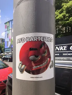 Street sticker A white square sticker depicting an angry red spherical character with clenched fists. The text 'AFD PARTEITAG' is written at the top, and 'widersetzen.com' is printed at the bottom.