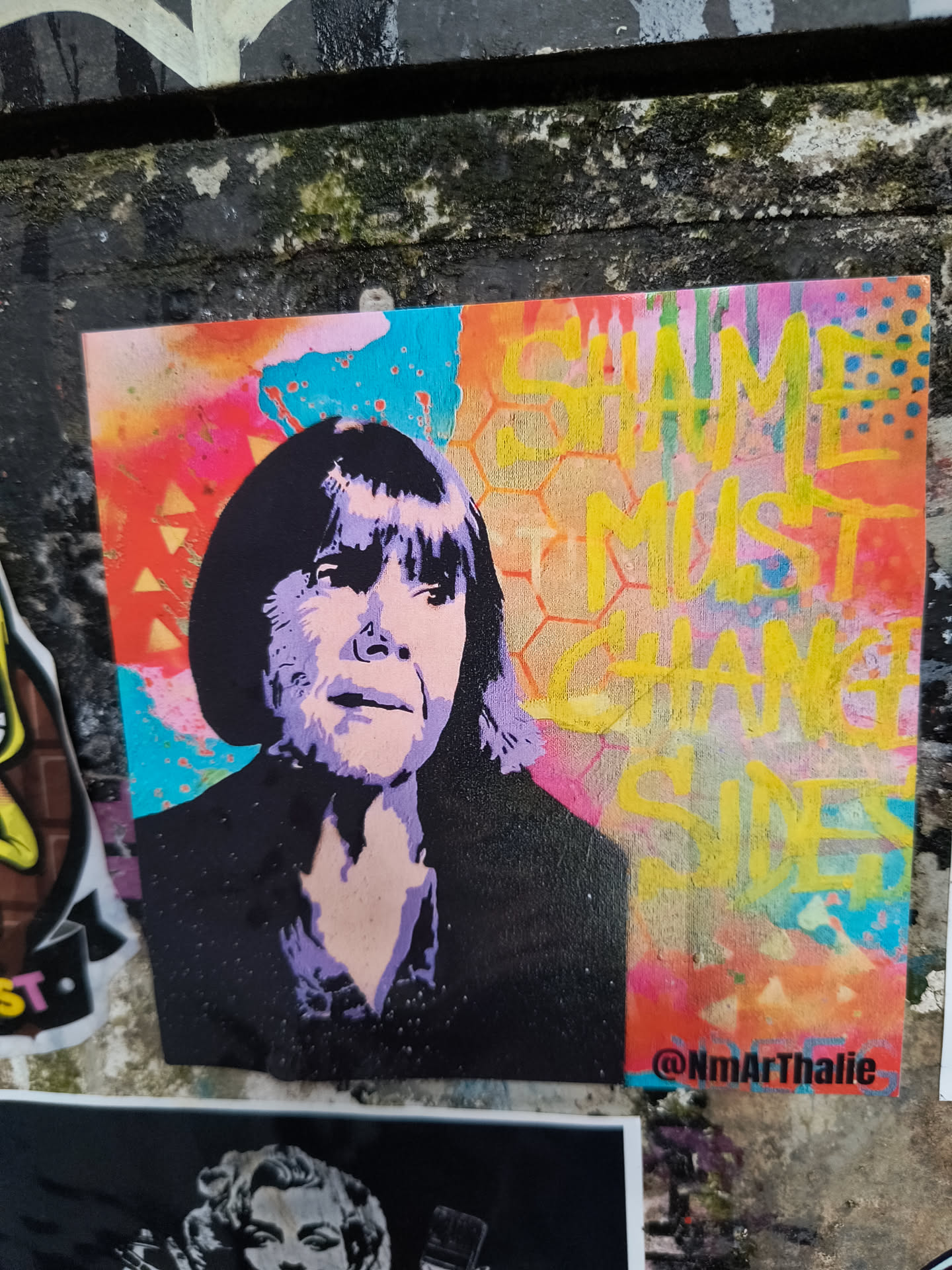 The sticker showcases a portrait of a woman with short dark hair and a determined expression, rendered in shades of purple and black against a colorful, abstract background. The right side of the sticker contains the phrase "GAME MUST CHANGE SIDES" in yellow, blocky letters, partially obscured by the colorful splatters and a hexagon pattern. The bottom right corner displays the handle "@NmArThalie".