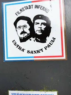 Street sticker A sticker featuring black and white portraits of Bertolt Brecht and Che Guevara, with text that reads 'Filmstadt Inferno Ultra Sankt Pauli'. The sticker has a tri-color design with blue, white, and red stripes.