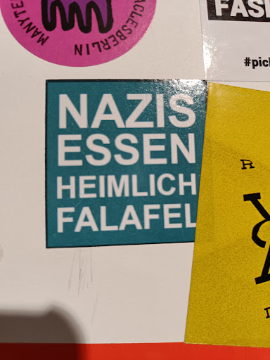 Street sticker A teal square sticker with white text that says Nazis Essen Heimlich Falafel.  It's a humorous statement suggesting a surprising food preference.