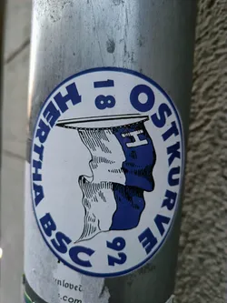 Street sticker A round sticker featuring the logo of Hertha BSC's Ostkurve (East Stand) fan group.  The logo incorporates the club's name and founding year (1892), with a visual element that appears to depict a profile of a head. The colors are primarily white and blue.