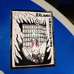 Black and white sticker depicting a topless woman sitting with a book in front of a burning building. The building has a Mercedes-Benz logo on top. The text "Ex libris counterculture" is written vertically on the sides.