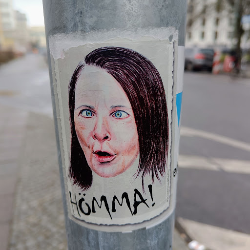 Street sticker A sticker depicting a woman with a surprised expression.  The word "Hömma!" is written below the image in a stylized font. The style is reminiscent of hand-drawn illustration or sketch.