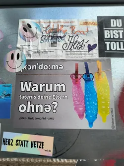 Street sticker A sticker with a provocative question in German, accompanied by an image of three condoms hanging on a clothesline. The overall style is simple and direct.