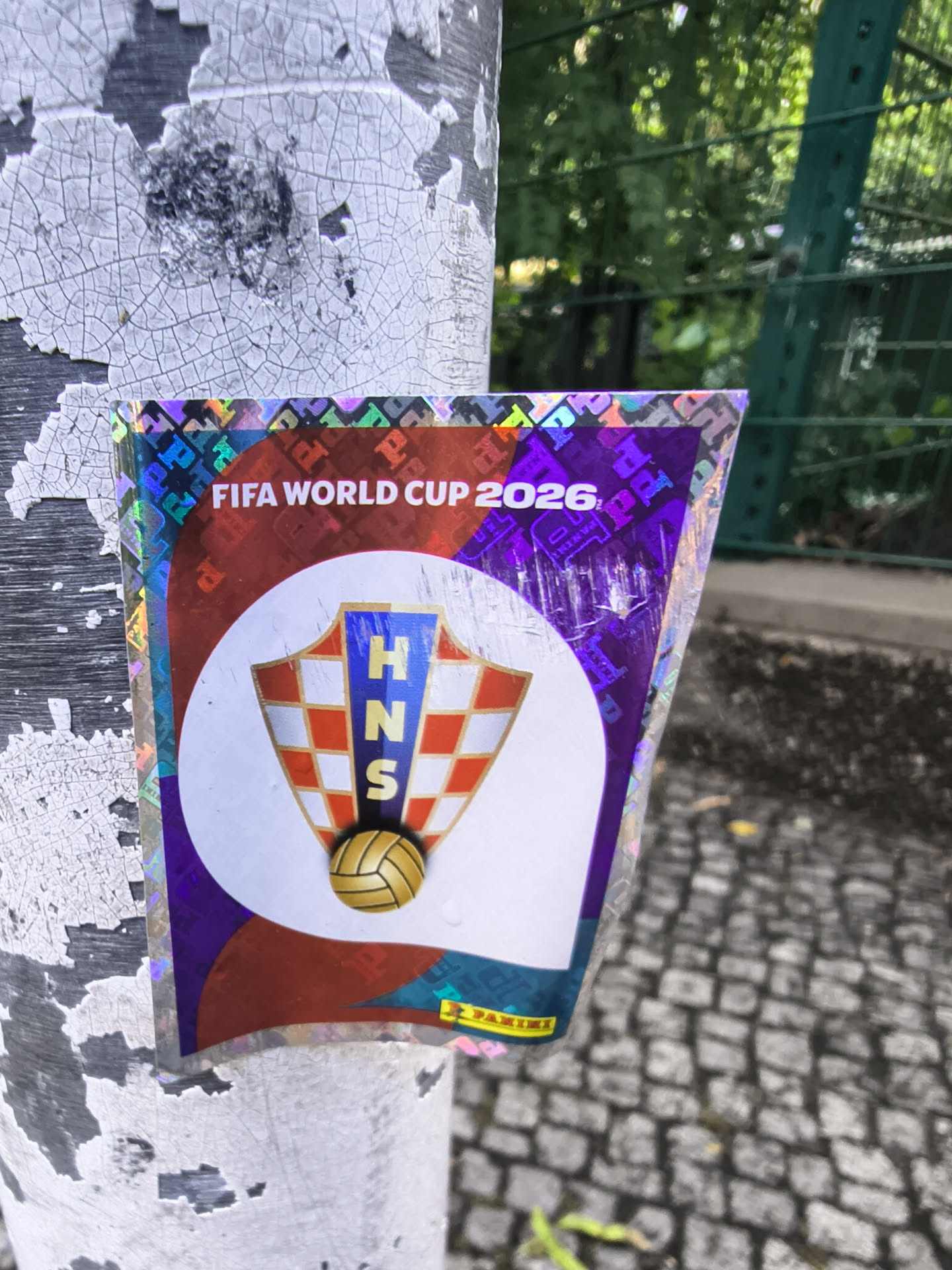 A holographic collectible sticker showing the Croatian Football Federation (HNS) crest on a white circular background. The crest features a red-and-white checkerboard pattern and a golden soccer ball. The background is metallic purple and red with 'FIFA WORLD CUP 2026' text at the top and a yellow Panini logo at the bottom.